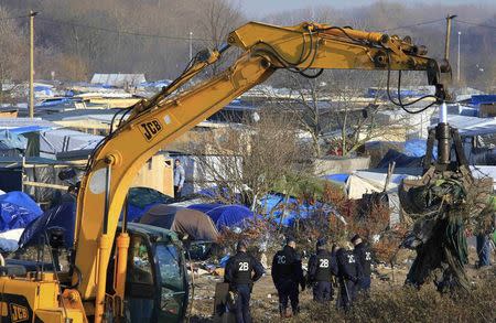 French police officers secure the area as a crane is used to clear dismantled shelters of the camp known as the "Jungle", a squalid sprawling camp in Calais, northern France, January 20, 2016. REUTERS/Pascal Rossignol