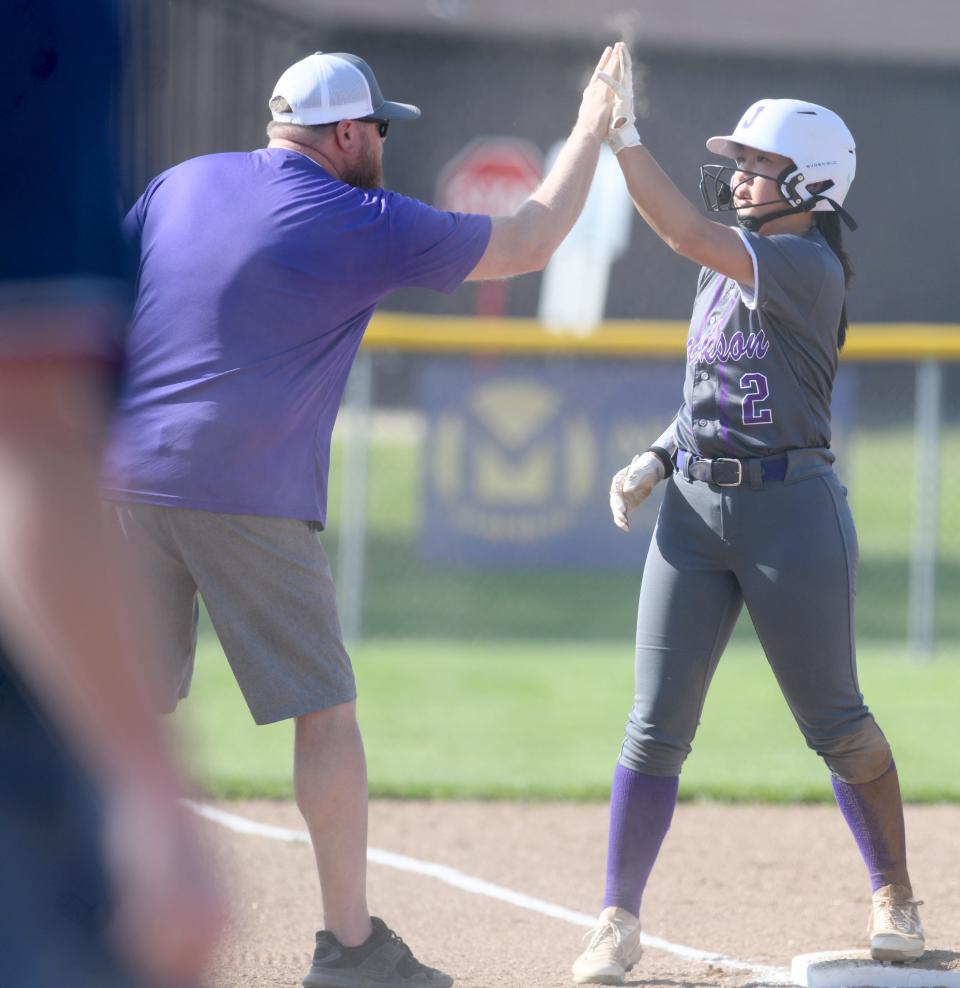 Jackson's Alexis Sin gives head coach Adam Parker a high-five after reaching third base in a Division I sectional final against Twinsburg, Wednesday, May 10, 2023.