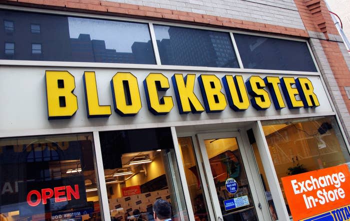 Storefront of Blockbuster with 'OPEN' sign and 'Exchange In-Store' ad visible