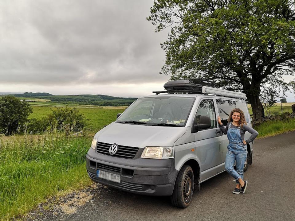 The writer in a field leaning on her gray van