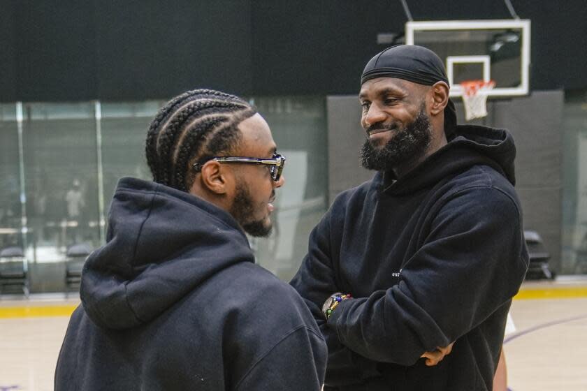 Bronny and LeBron James smile while standing and looking at each another on the court at the Lakers practice facility