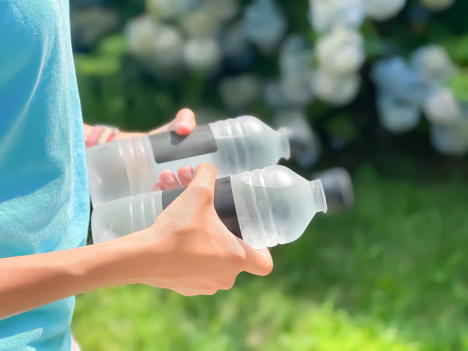 teenager holding two cold bottles of water while walking outdoors