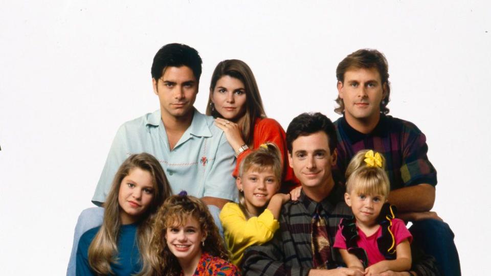 john stamos sitting for a cast photo with the actors of full house