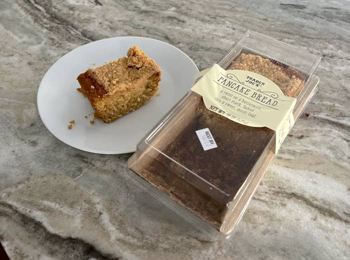 A slice of cake on a plate beside its packaging labeled "Vintage Bread Pineapple Bread" on a marble surface