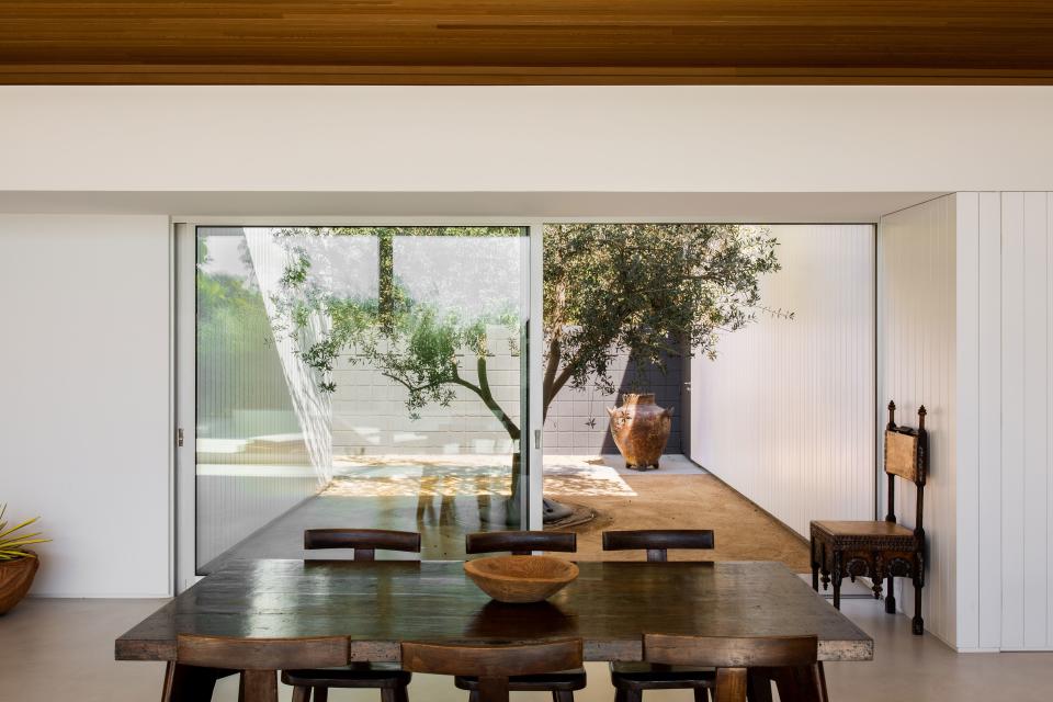 The home was designed so that the interior flows seamlessly into the exterior. Nowhere is this more apparent than the dining room, where a large sliding door looks out onto a picturesque olive tree. The table is a 1930s Pierre Jeanneret, the chairs are 1950s Olavi Hanninen, and the chair against the wall is by Carlo Bugatti and dates to 1906.