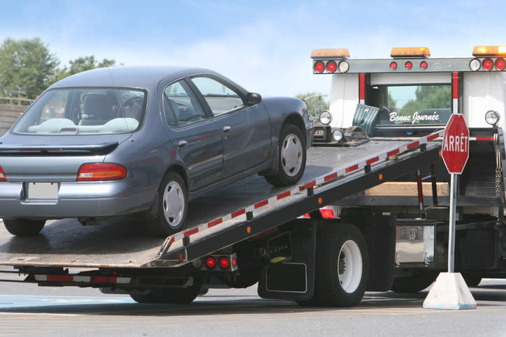 A car being towed onto a flatbed tow truck with an "Arret" sign, French for "Stop," visible