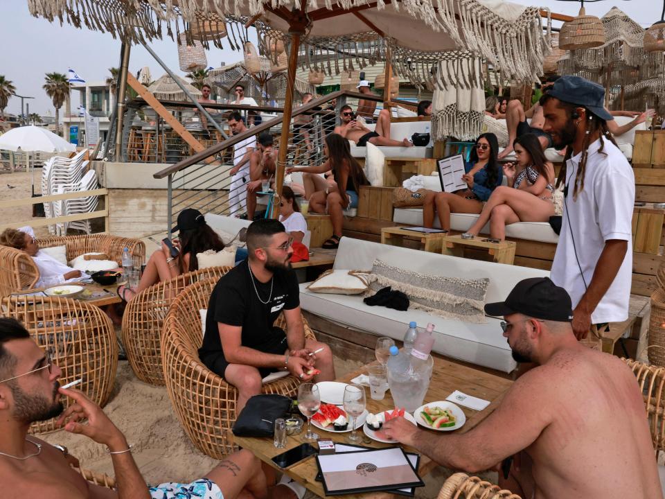 People relax at a beach bar in the Israeli coastal city of Tel Aviv on 19 April after authorities announced face masks were no longer needed outside (AFP via Getty Images)