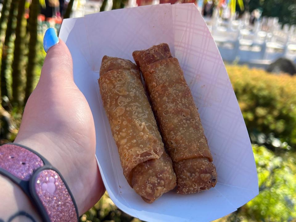 hand holding a takeout boat of pork egg rolls in epcot in disney world