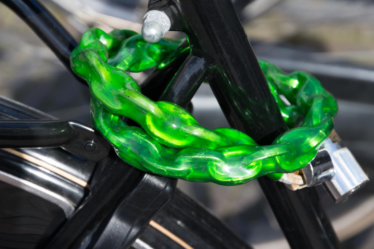 Black bicycle parked on the street protected with a heavy green bike lock.