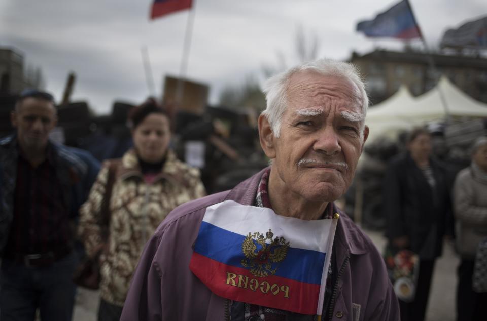 A man holds a Russian national flag as he and the others listen to a pro-Russian activist at barricades in front of a regional administration building that was seized by pro-Russian activists earlier in Donetsk, Ukraine, Sunday, April 20, 2014. The Ukrainian and Russian governments are reporting a shootout at a checkpoint set up by pro-Russian insurgents in eastern Ukraine that has left one person dead and others hospitalized with gunshot wounds. (AP Photo/Alexander Zemlianichenko)