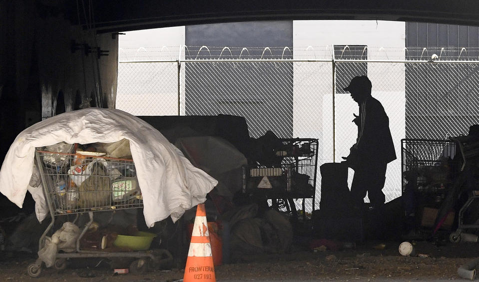 FILE - In this May 21, 2020 file photo, a man is seen at a homeless encampment that sits under Interstate 110 near Ramirez Street during the coronavirus outbreak in downtown Los Angeles.A judge has approved an agreement in which the city and county of Los Angeles will provide housing for almost 7,000 homeless people who live near freeways. Officials said Thursday, June 18, 2020 the city will provide 6,000 new beds within 10 months and another 700 beds over 18 months. Meanwhile the county will spend $300 million over five years to fund services for the people. (AP Photo/Mark J. Terrill, File)