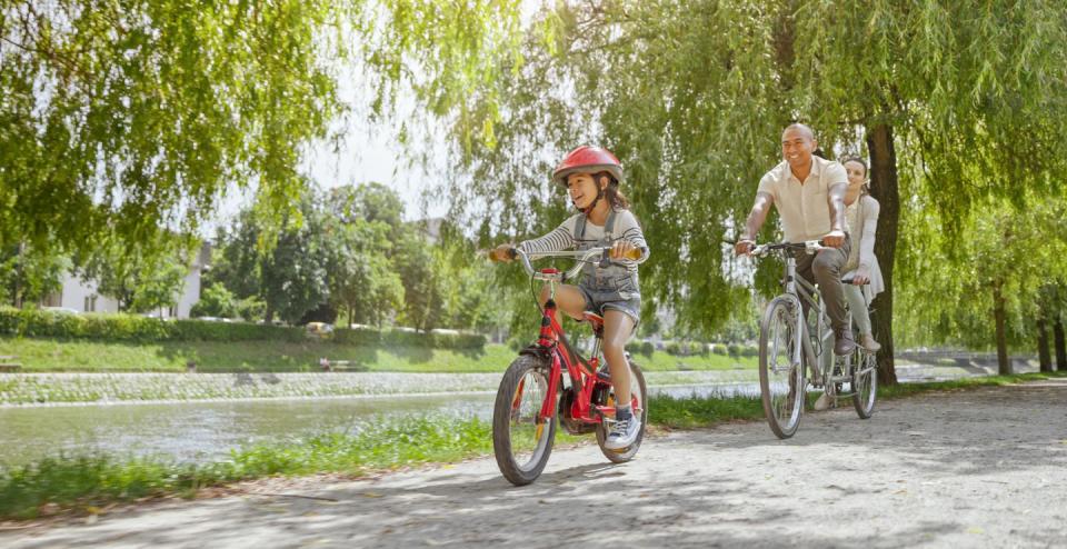 smiling family riding bicycle together on footpath by lake in public park