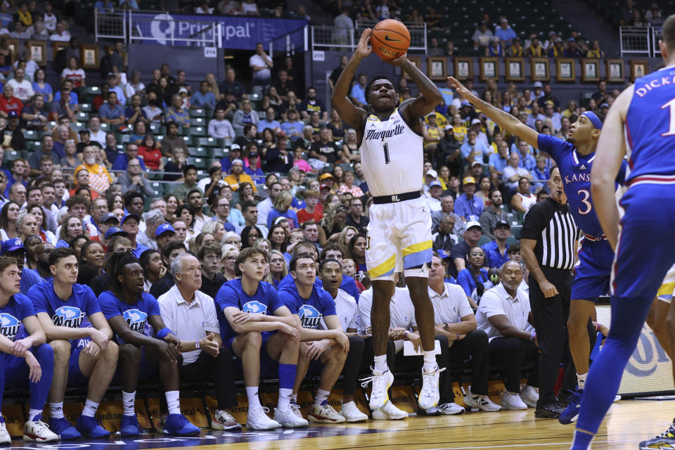 Marquette guard Kam Jones (1) attempts a 3-pointer in front of the Kansas bench during the first half of an NCAA college basketball game Tuesday, Nov. 21, 2023, in Honolulu. (AP Photo/Marco Garcia)