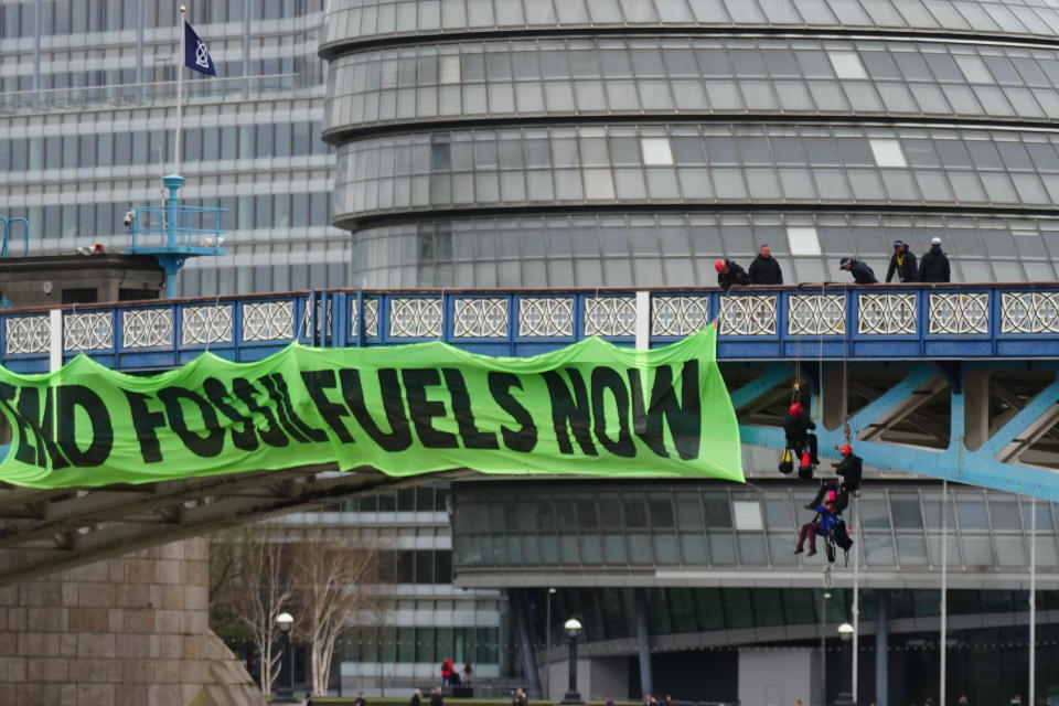 Police officers work to remove activists from Extinction Rebellion who are hanging from suspension cords beside a giant banner that reads 