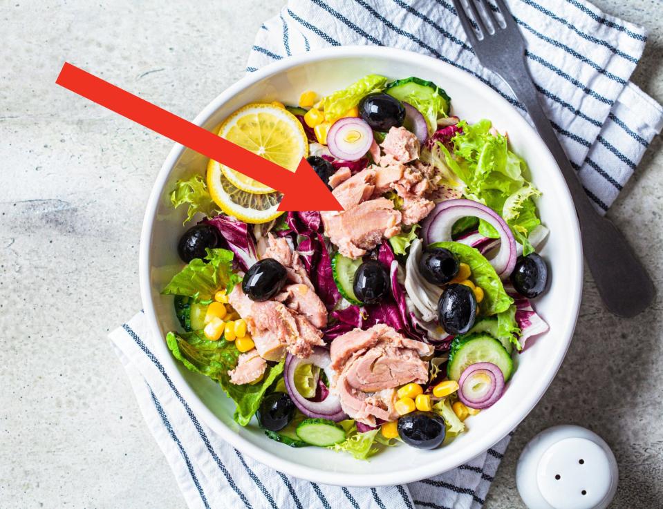 Tuna salad with cucumbers, corn, olives and red onions in a white bowl.