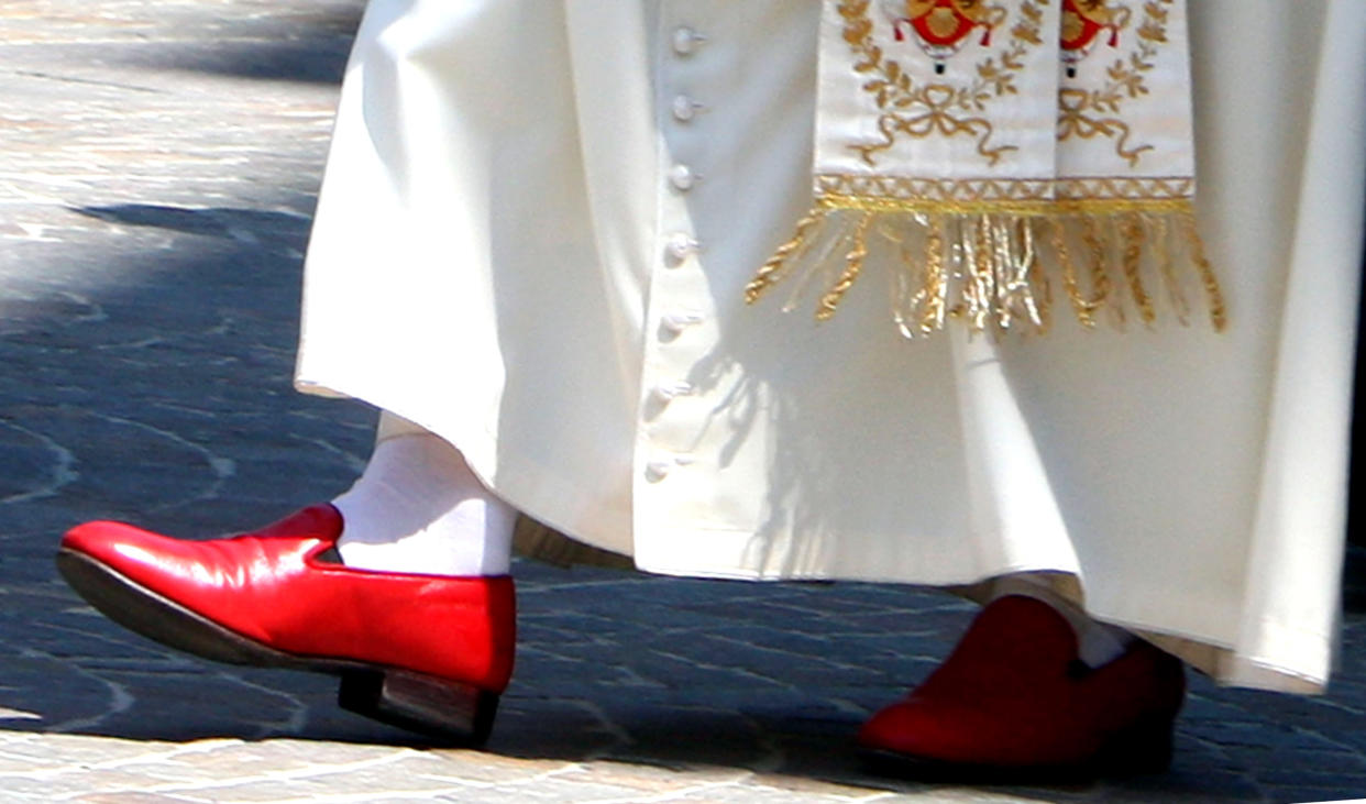 Close-up from the knees down of someone wearing a vestments, white socks and red shoes.