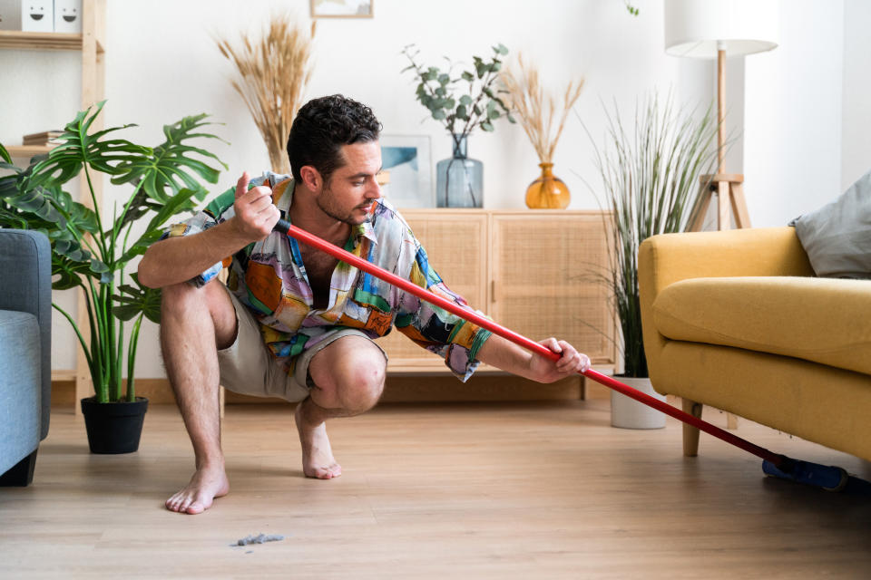 A man sweeping under the couch