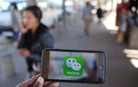 A WeChat logo is displayed on a mobile phone as a woman walks past as she talks on her mobile phone at a taxi rank in this picture illustration taken July 21, 2016. Picture taken July 21, 2016. REUTERS/Siphiwe Sibeko/Illustration