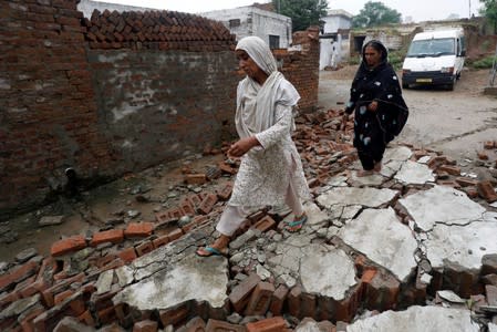 Women walk over rubbles of a damaged wall after an earthquake in Jatlan, Mirpur