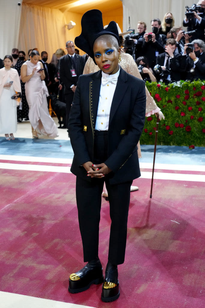 Janicza Bravo wearing a slim fitting tux, dramatic eye makeup, and a uniquely shaped hat