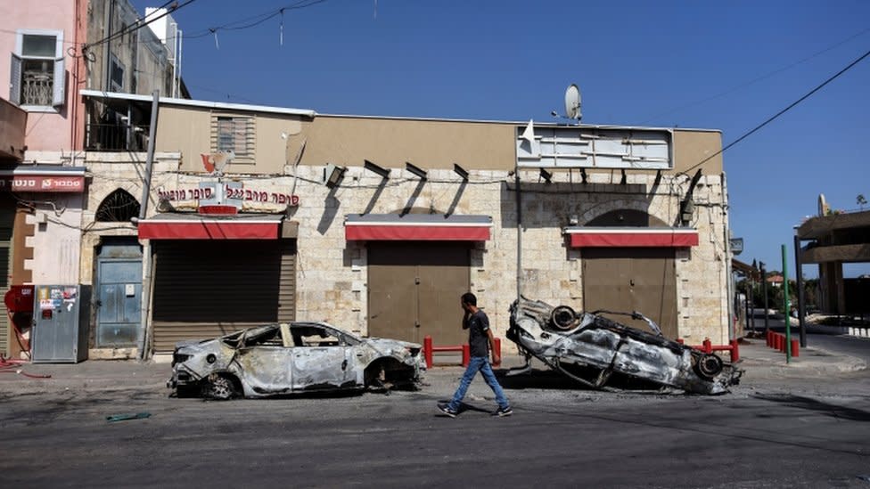 Un hombre camina, pasando dos vehiculos incendiados en la ciudad israelí de Lod.