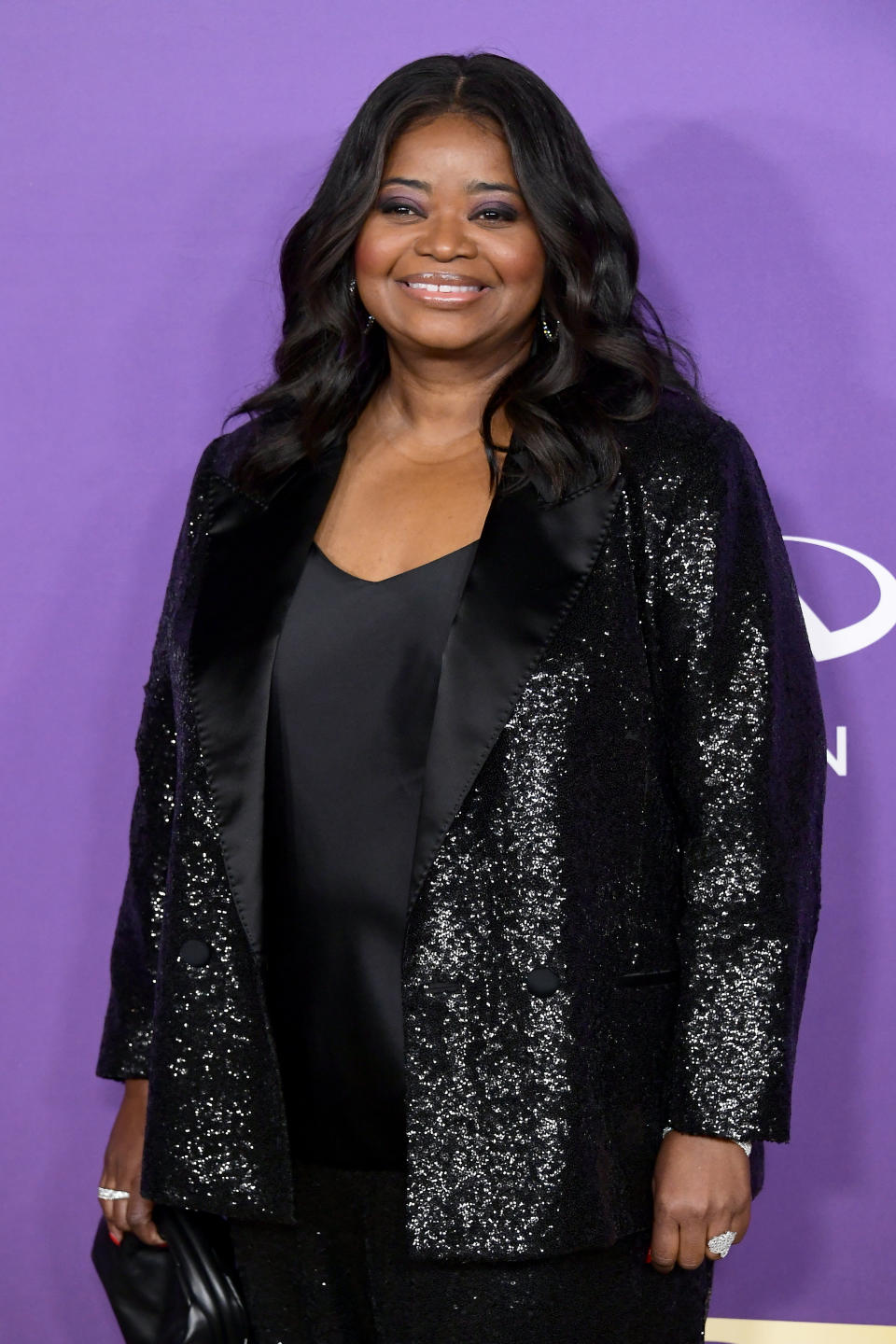 Octavia Spencer on the purple carpet in a sparkly black jacket and black top, smiling