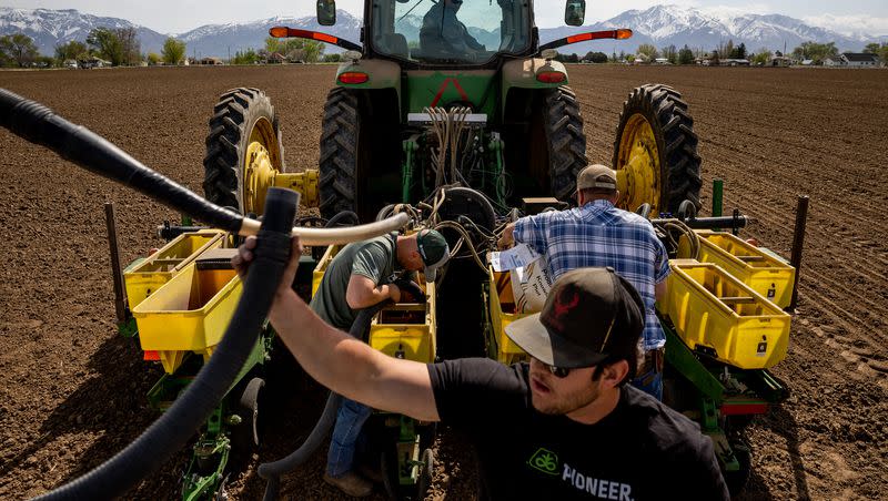 Ron Gibson, owner of Gibson’s Green Acres and president of the Utah Farm Bureau, looks down from the pilot seat of his tractor while Landon Potter, Wyatt Monroe and Shane Monroe switch between different varieties of corn seed in a planter on Gibson’s farm in Ogden on Thursday, May 4, 2023.