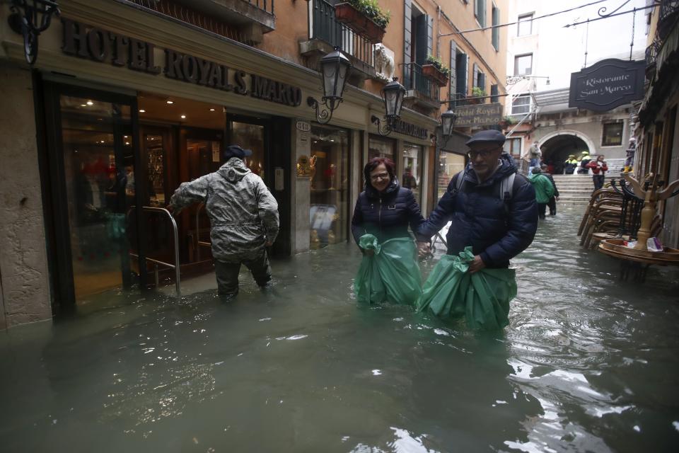 People wade their way through water in Venice, Italy, Friday, Nov. 15, 2019. Waters are rising in Venice where the tide is reaching exceptional levels just three days after the Italian lagoon city experienced its worst flooding in more than 50 years. (AP Photo/Luca Bruno)