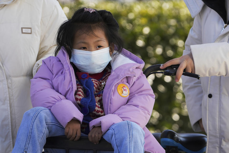 A child wearing a face mask to help protect from the coronavirus sits on a bike in Beijing, Tuesday, Feb. 8, 2022. China has ordered inhabitants of the southern city of Baise to stay home and suspended transportation links amid a surge in COVID-19 cases at least partly linked to the omicron variant. (AP Photo/Andy Wong)