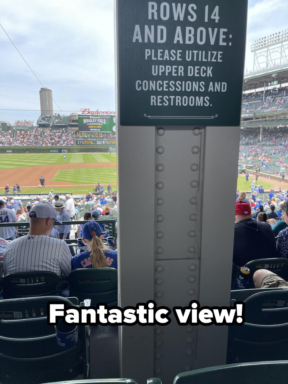 A sign at a baseball game says, "Rows 14 and above: Please utilize upper deck concessions and restrooms." Fans are seated in the stadium, and the game is ongoing