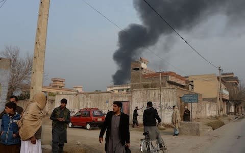 Afghan civilians gather on a street next to a plume of smoke coming from the area around an office of the British charity Save the Children during an ongoing attack in Jalalabad - Credit: NOORULLAH SHIRZADA /AFP