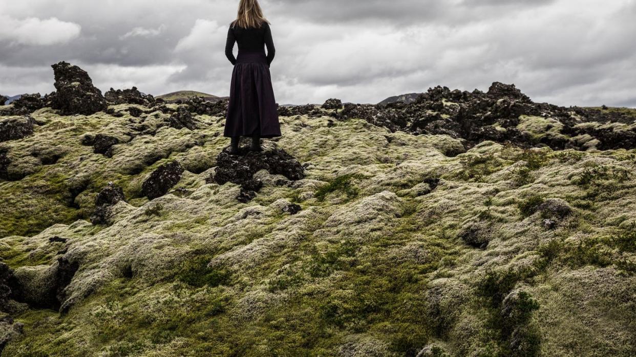 lonely woman walking on mossy lavafield
