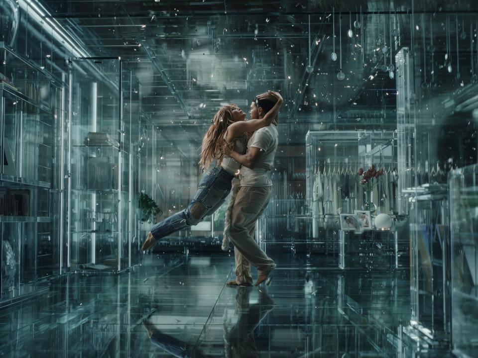 jennifer lopez embraces a man in a blue space that looks like a tech simulation of a nice bedroom