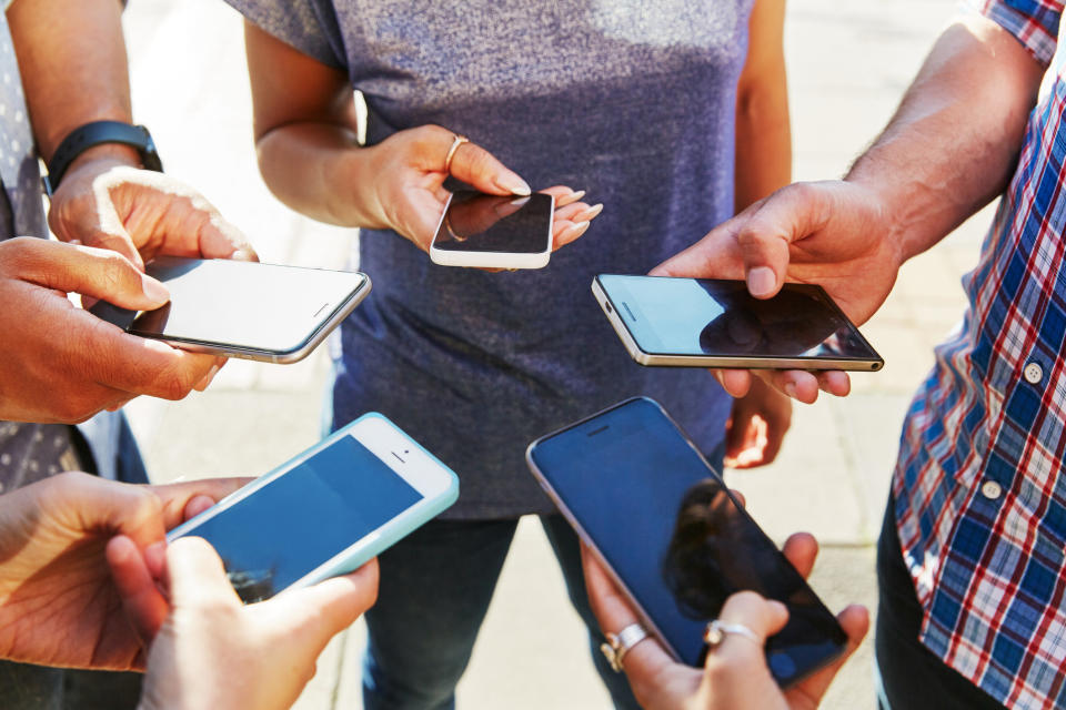 A group of hands holding smartphones in a circle.