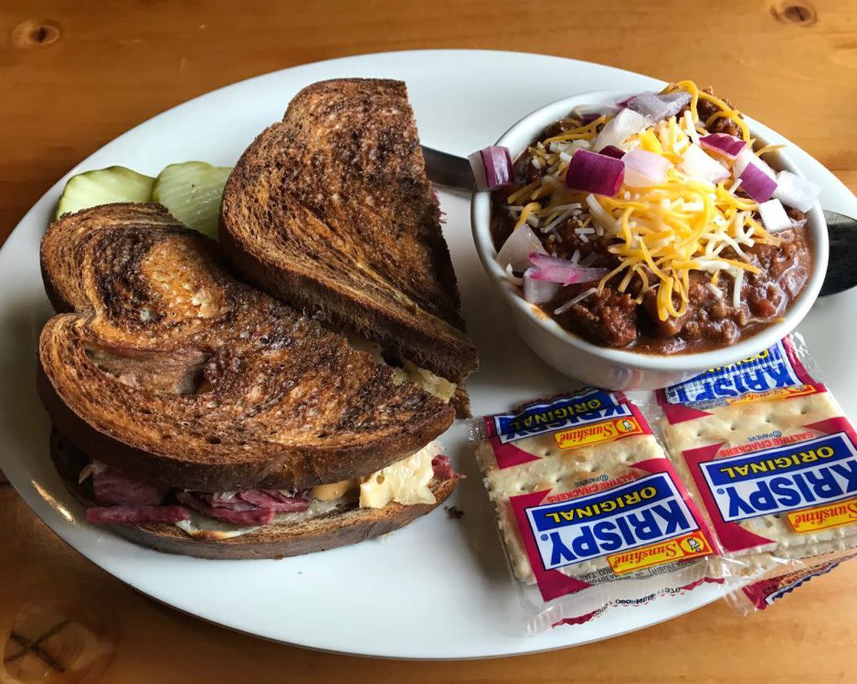 Reuben Sandwich with a bowl of chili and two packs of crackers on a white porcelain plate with a spoon, The Crescent Moon Ale House, Omaha, on a rustic wooden table