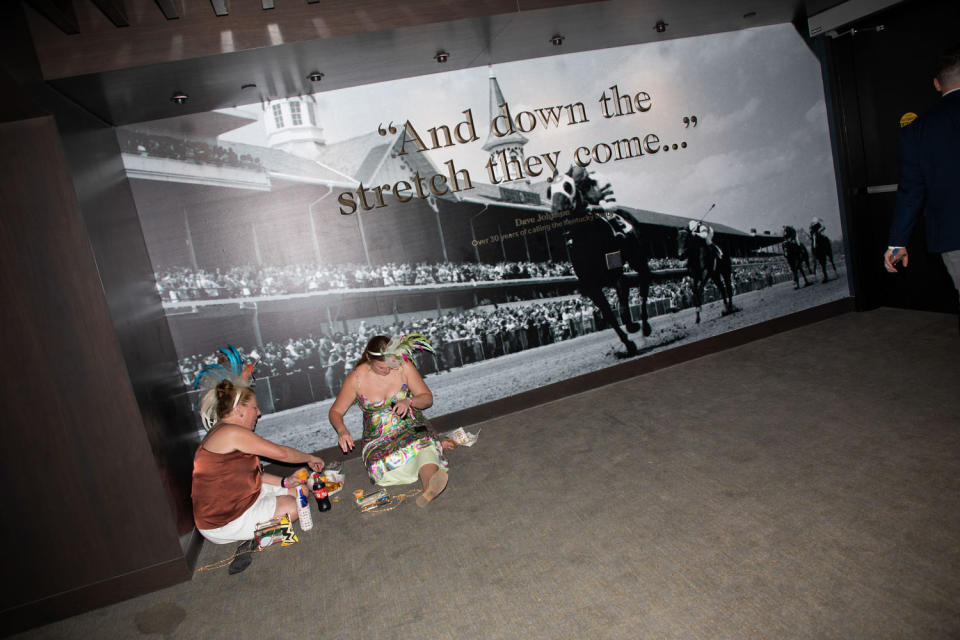 Two women eat near a sign at Churchill Downs that reads 