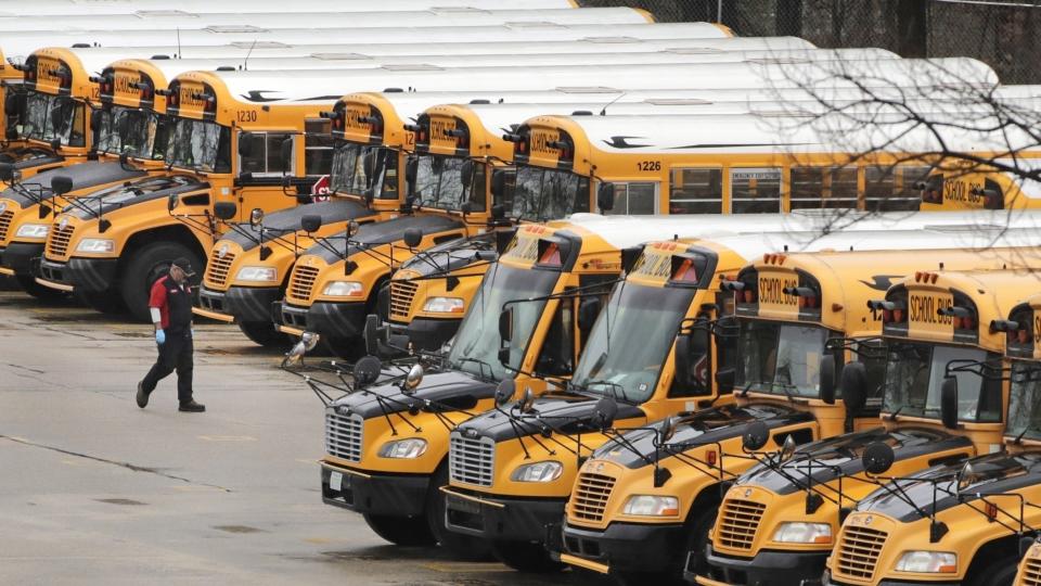 FILE - In this April 27, 2020, file photo, a worker passes public school buses parked at a depot in Manchester, N.H. Reopening schools during the coronavirus pandemic means putting children on school buses, and districts are working on plans to limit the risk. (AP Photo/Charles Krupa, File)