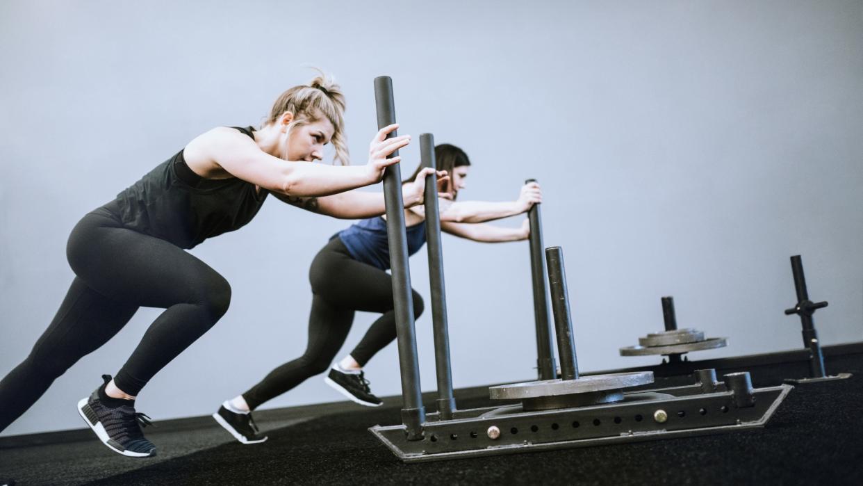  Two women performing sled push during workout. 