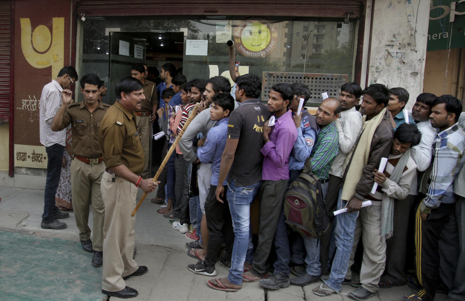 FILE- An Indian police officer warns people against breaking the queues as they wait to exchange or deposit discontinued currency notes, outside a bank on the outskirts of New Delhi, India, Nov. 15, 2016. In November 2016, India withdrew all 500-rupee and 1,000-rupee from circulation, in an effort to tackle corruption, black money and tax evasion. India’s top court hearing petitions challenging the currency ban on Monday, Jan.2. 2013 said the government’s surprise decision in 2016 to demonetize high-value bills was legal and taken after consultation with India's central bank. (AP Photo/Altaf Qadri, File)