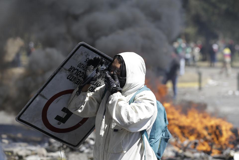 An anti-government demonstrator takes cover with a traffic sign during clashes with police in Quito, Ecuador, Saturday, Oct. 12, 2019. Protests, which began when President Lenin Moreno's decision to cut subsidies led to a sharp increase in fuel prices, have persisted for days. (AP Photo/Fernando Vergara)