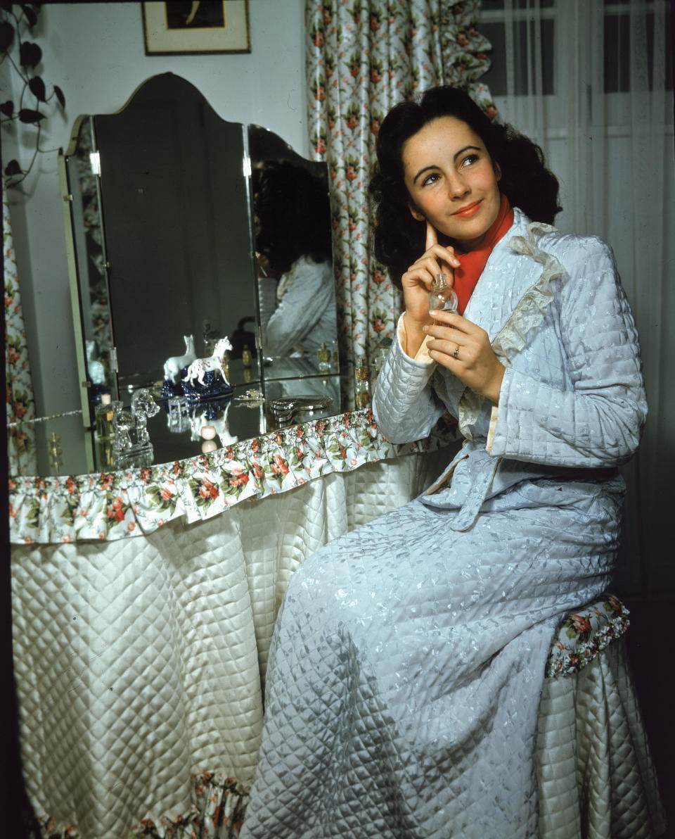 Taylor sits at a mirror-topped vanity table and applies perfume, circa 1940s.&nbsp;