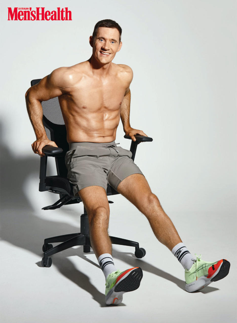 Ed Cavalee sitting in a desk chair, wearing grey shorts and sneakers, no shirt.