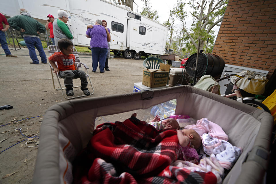 Two-week old twins Lilly and Zoey lay in a bassinet as Hannah Bourque hugs church volunteers who brought Christmas presents to her son Conner, seated, outside the camper she is living in with her grandfather, while her mother lives in a tent in the backyard of their heavily damaged home, in the aftermath of Hurricane Laura and Hurricane Delta, in Lake Charles, La., Friday, Dec. 4, 2020. (AP Photo/Gerald Herbert)