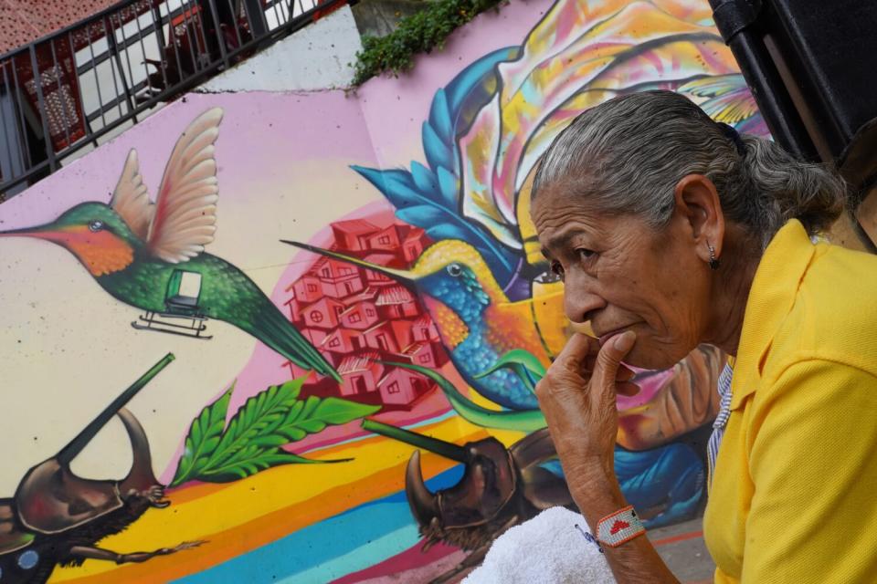 A woman sits in front of a colorful mural.