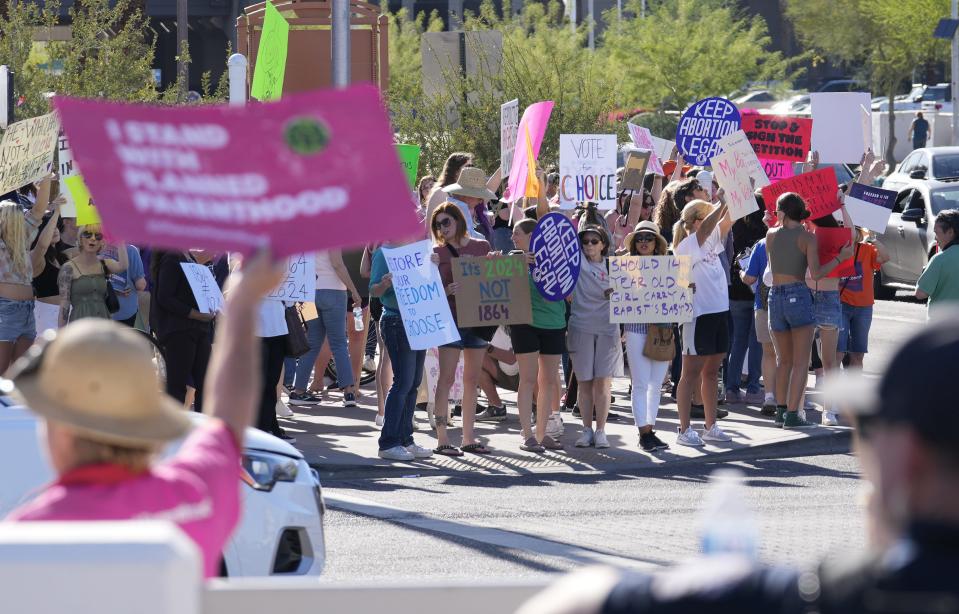 Demonstrators hold signs against the 1864 near-total territorial abortion ban while protesting in Scottsdale on April 14, 2024.