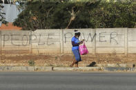 A woman walks past a wall with graffiti advocating for the empowerment of people in the streets of Harare, in this Tuesday, June, 9, 2020 photo. Unable to protest on the streets, some in Zimbabwe are calling themselves "keyboard warriors" as they take to graffiti and social media to pressure a government that promised reform but is now accused of gross human rights abuses.(AP Photo/Tsvangirayi Mukwazhi)