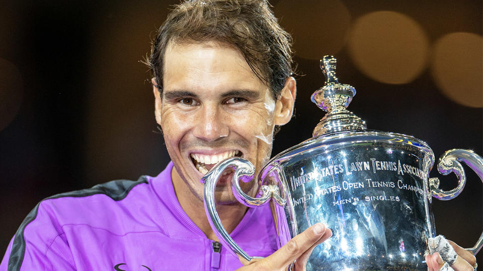 Rafael Nadal biting the US Open trophy and smiling.