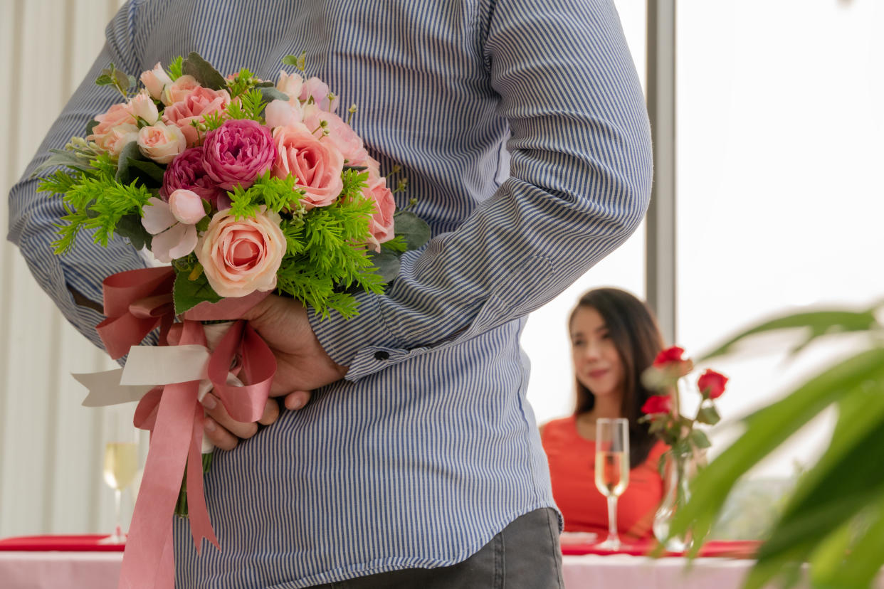 Asian man hiding flower to surprise his girlfriend on dating in Valentine's, Anniversary or birthday, focus on happy woman smile on face, attractive couple having dinner together