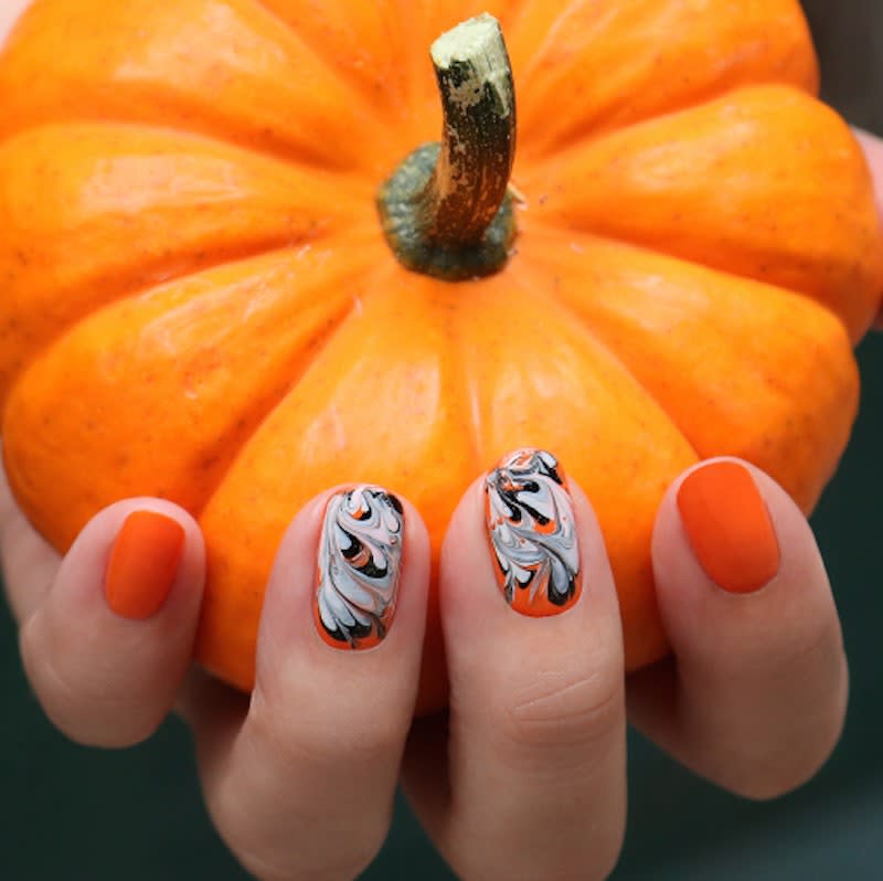 <a href="https://jinsoon.com/content/fancybox/Tutorials/Halloween.jpg" rel="nofollow noopener" target="_blank" data-ylk="slk:This manicure;elm:context_link;itc:0;sec:content-canvas" class="link ">This manicure</a> conveys a clear love of Halloween without screaming it like a banshee. After a perfect pumpkin-orange base in the JinSoon shade Enflammee. While it's still wet, the shades Obsidian and Doux were added to two accent nails and gently dragged with a striping brush to create ghostly swirls.