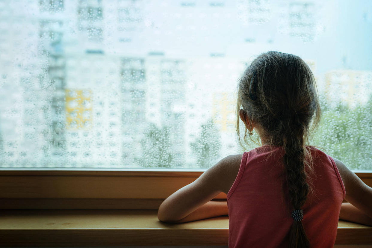 Little sad girl pensive looking through the rainy window. Getty Images/Train_Arrival
